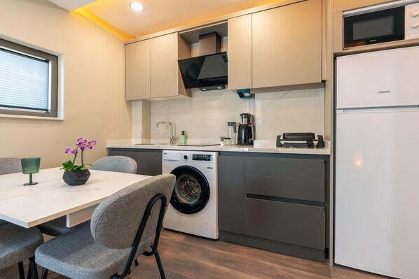 Una cocina compacta con lavadora integrada, microondas y refrigerador.