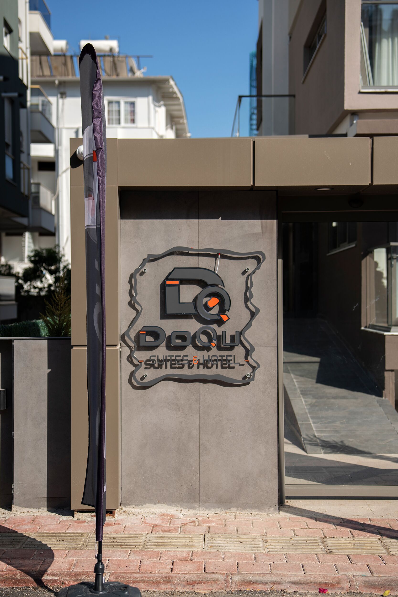 A building with a sign for 'DQU Hotel' featuring a stylized logo and the words 'Suites & Hotel'.