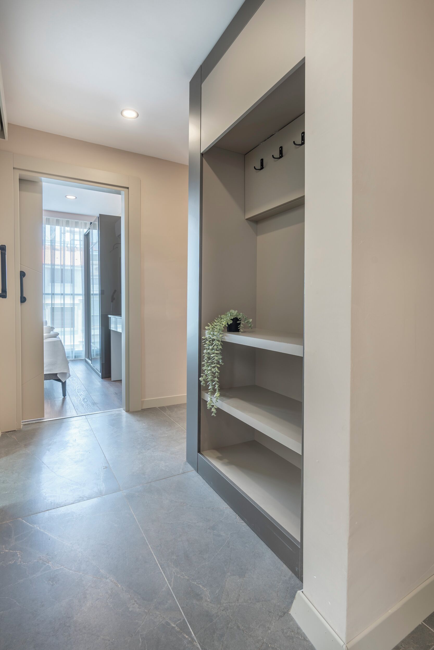 Ein Flur mit modernem Design, ausgestattet mit einer eingelassenen Deckenleuchte, einer Tür zu einem Zimmer mit Blick und einer Wandablage mit Haken und einer kleinen Pflanze.