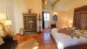 Een slaapkamer met een groot bed, een houten garderobe, een rustieke kast en een klein tafeltje met een lamp.