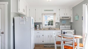 A kitchen with white cabinets, a refrigerator, a stove, and a dining table with chairs. - Pelican's Nest - Soundside, 5 min to beach, 2BR 1BA, Atlantic Beach (Atlantic Beach)