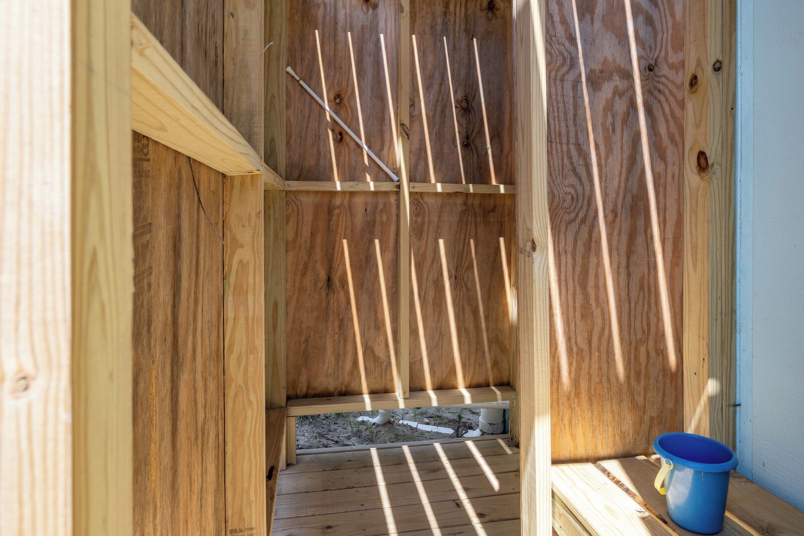 A wooden structure with a sloped roof and a blue bucket on the right.