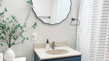 A bathroom with a white sink, dark blue vanity, a round mirror, a shower curtain, and a plant on the counter.