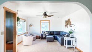 A modern living room with a sectional sofa, a white armchair, a small side table, and a ceiling fan. - Beautiful cozy country home located on 12 acres in a great farming community. (Hancock)