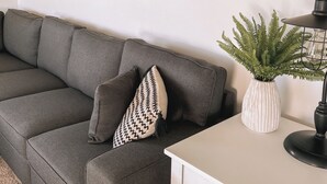 A modern living room with a grey sofa, a white side table, a black lamp, and a decorative wall hanging. - Beautiful cozy country home located on 12 acres in a great farming community. (Hancock)
