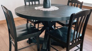 A round dining table with a dark finish, surrounded by four black chairs with cushioned seats. A vase with dried flowers is placed on the table's center. - Beautiful cozy country home located on 12 acres in a great farming community. (Hancock)