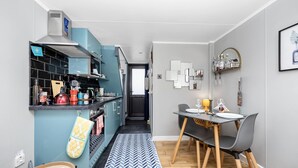 A modern kitchen with blue cabinets, a dining area with a table and chairs, and a hallway leading to a bedroom.