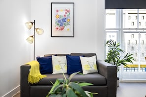 Relax in this stylish living room with a sofa, throw blanket, and floor lamp, offering a view of the city.