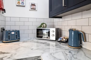 Kitchen features a microwave, toaster, and kettle on a countertop, with a small plant adding a touch of greenery.