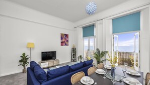 Una sala de estar moderna con un sofá azul, una mesa de comedor lista para cuatro personas y un televisor sobre un mueble de madera.
