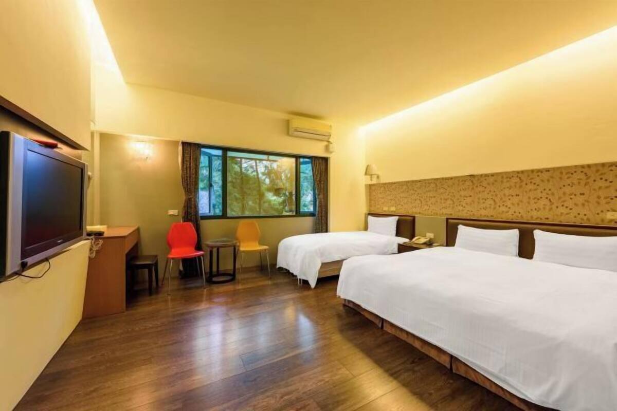 Habitación de hotel con dos camas, un escritorio, una silla y un televisor.
