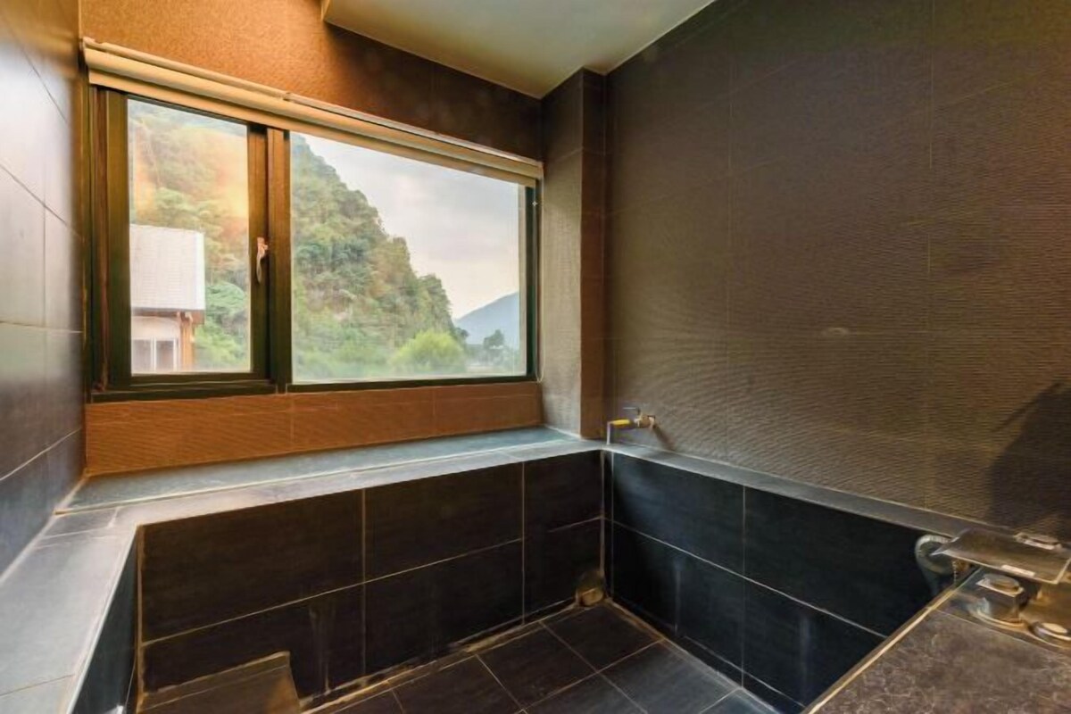 Un bagno con finestra, piastrelle scure e una vasca da bagno.