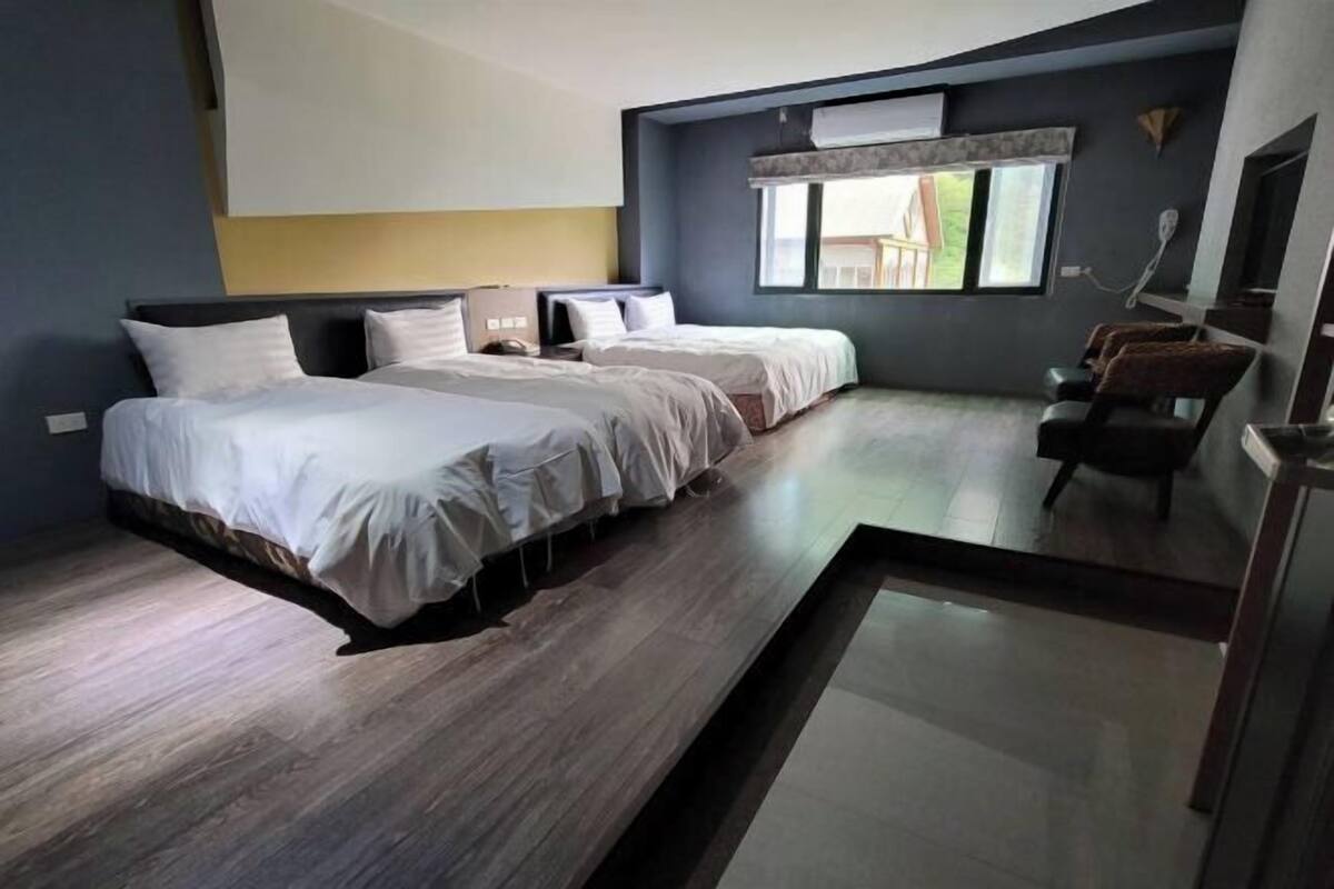Una habitación de hotel moderna con dos camas, un pequeño rincón de descanso y un ventanal grande.