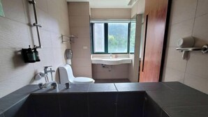 A modern bathroom with a dark tiled sink, a toilet, and a window providing natural light. - Xiang Ting (Nantou)