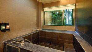 A modern bathroom with a large bathtub, a window with a view of greenery, and two bottles of shampoo on the wall. - Xiang Ting (Nantou)
