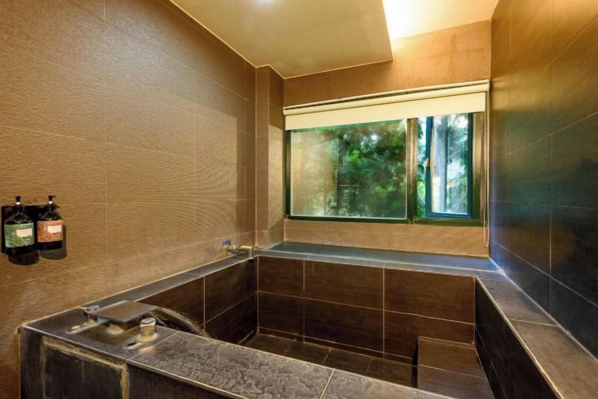 Un bagno moderno con una vasca da bagno grande, una finestra vista verde e due flaconi di shampoo a parete.