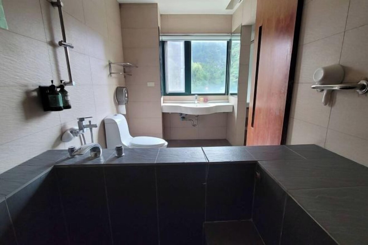 Un bagno moderno con un lavandino rivestito di piastrelle scure, un WC e una finestra che lascia entrare luce naturale.