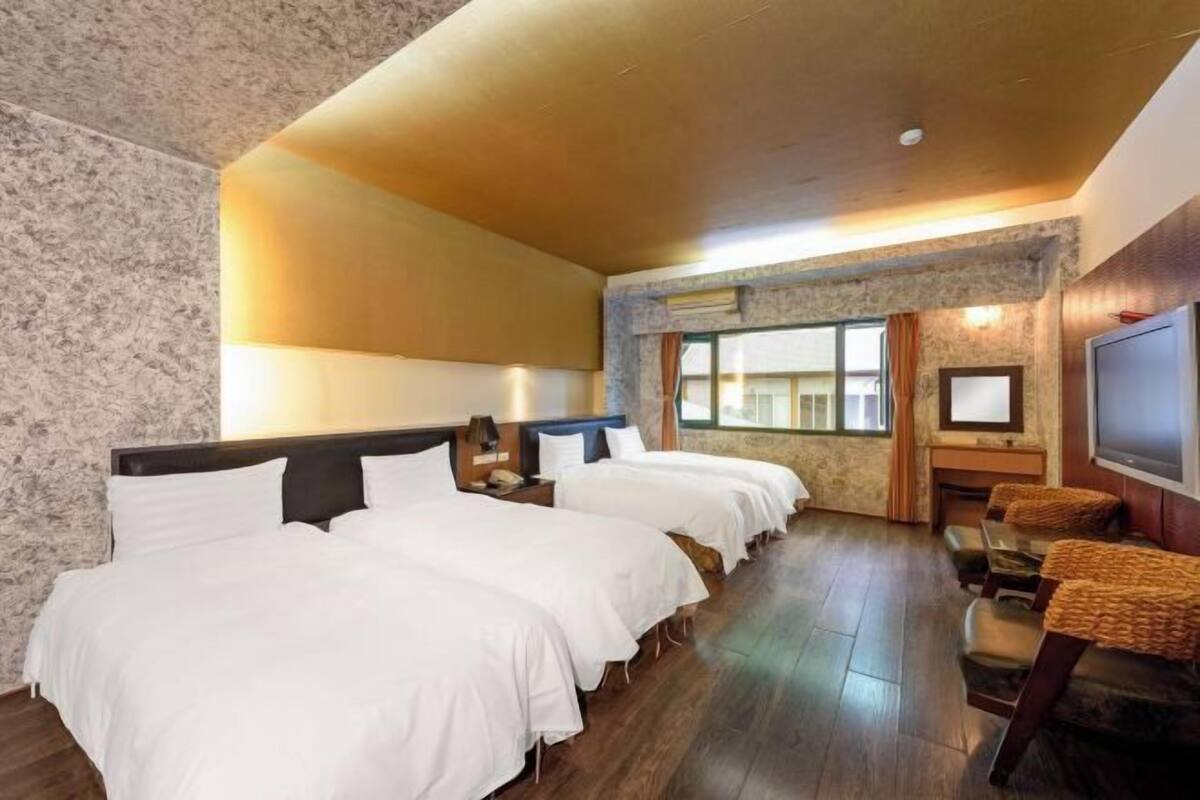 Habitación de hotel con tres camas, televisión y una zona de estar con sillas.