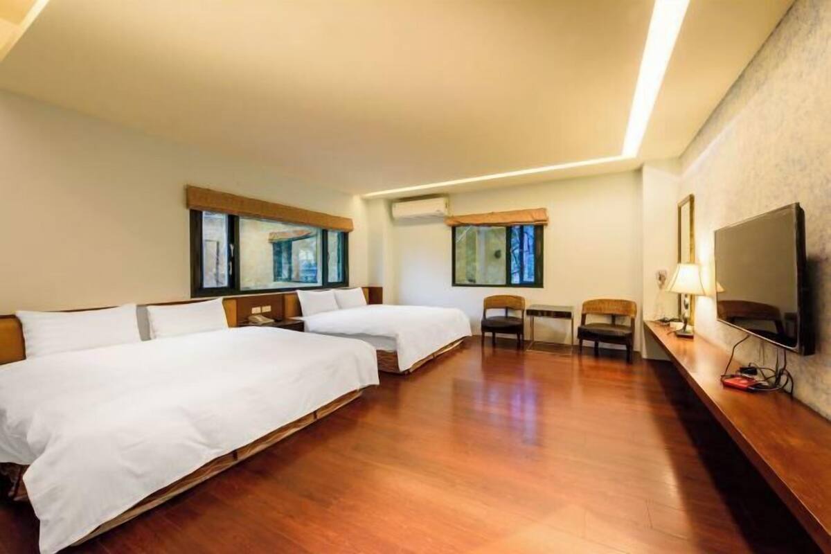 Habitación de hotel con dos camas, un escritorio con lámpara, televisión y ventana con cortinas.