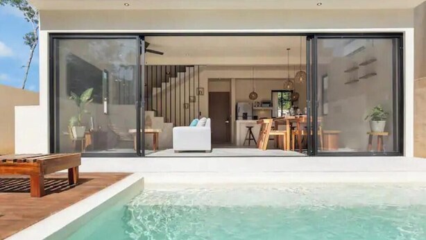Et moderne hus med swimmingpool, spiseområde og køkken, som kan ses gennem store glasdøre.