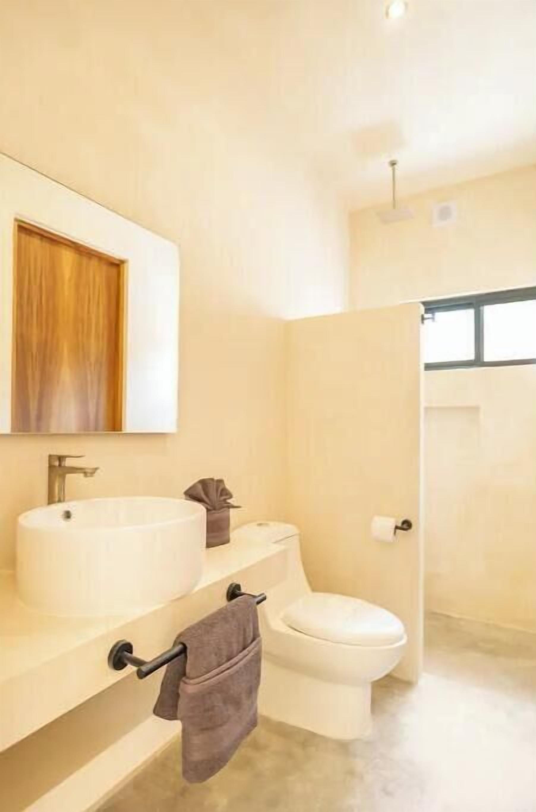 Un baño moderno con un espejo grande, un lavabo redondo, un inodoro y un perchero para toallas.