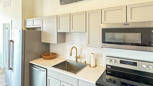 Una cocina moderna con un refrigerador de acero inoxidable, un lavavajillas integrado, un lavamanos con grifo dorado, un microondas y un horno.