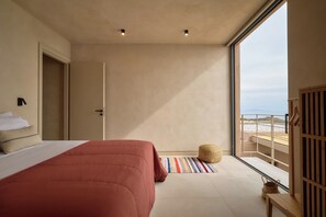 A bedroom with a large bed, a view of the beach, and a balcony with a wooden railing.