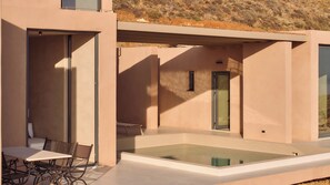 A modern outdoor patio with a glass-top table and chairs, a small seating area, and a water feature.