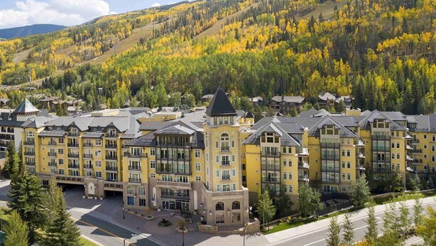 A multi-story hotel with a central courtyard, surrounded by autumn-colored trees and a mountainous backdrop.