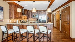 A kitchen with wooden cabinets, a central island with bar stools, stainless steel appliances, and pendant lighting.