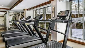 A gym with treadmills, exercise equipment, and large windows with a view of snow outside.