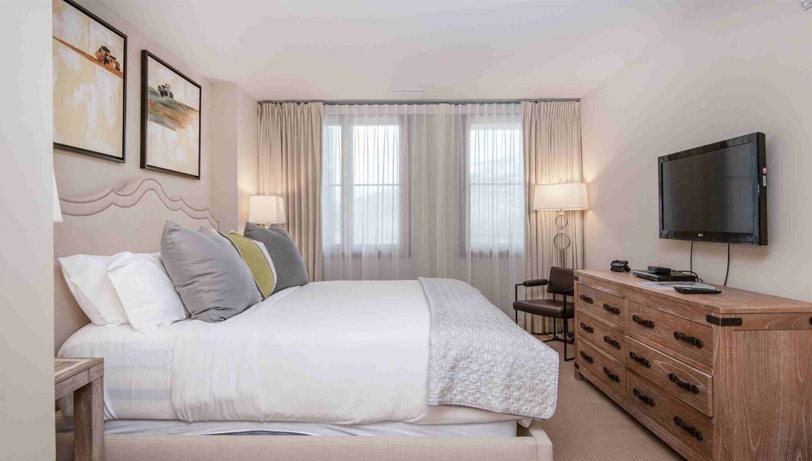Een hotelkamer met een groot bed, een houten dressoir, een televisie en twee afbeeldingen in lijsten aan de muur.