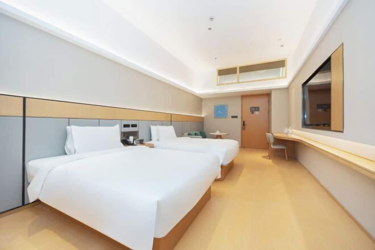 Quarto de hotel com duas camas, uma escrivaninha, uma cadeira, um espelho e uma mesinha.