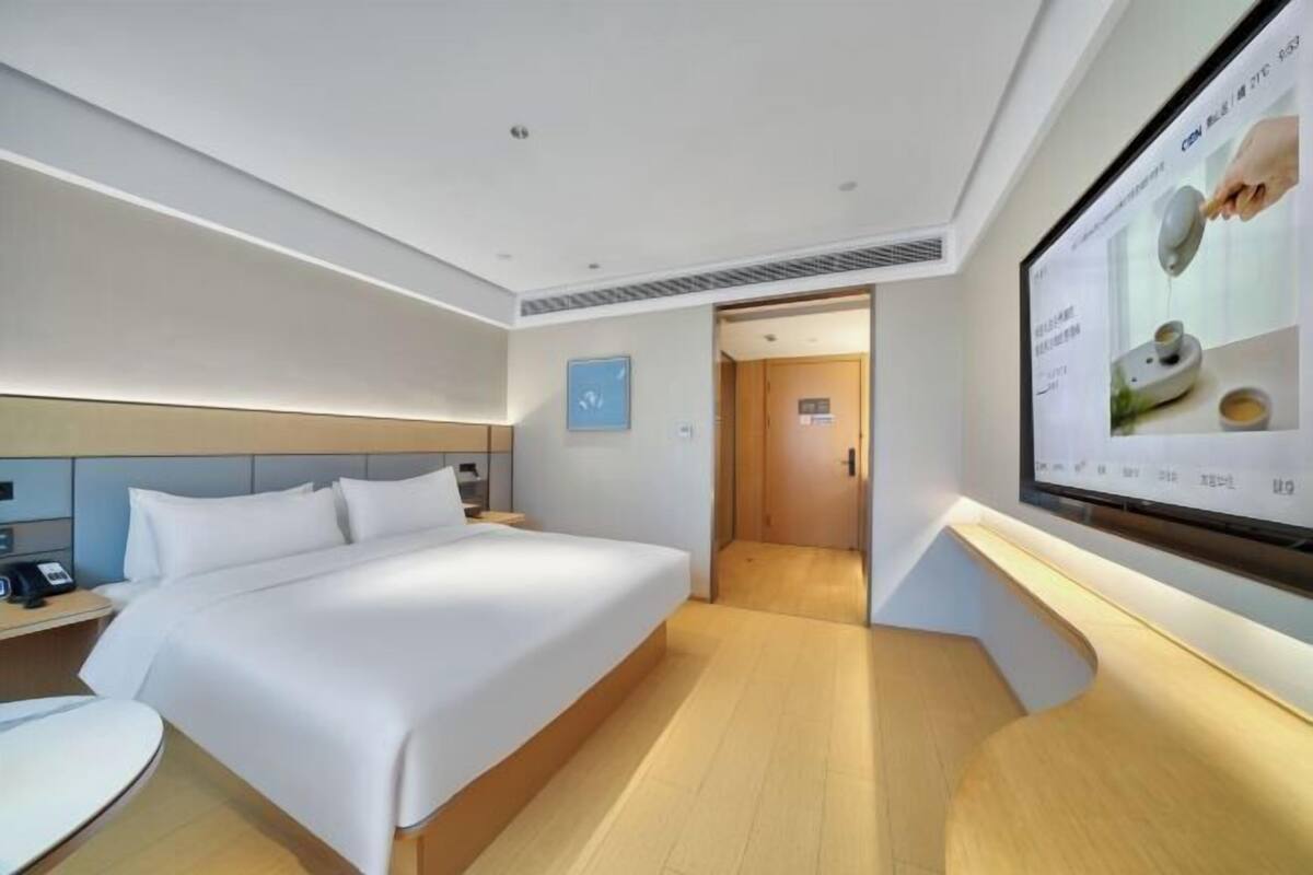 Quarto de hotel com cama, mesa de cabeceira, televisão e porta que dá para outro cômodo.