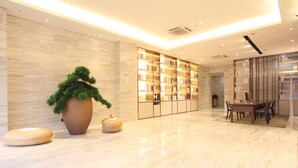 A modern lobby with a marble floor, a large potted plant, a seating area, and a wall with a built-in bookshelf. - Ji Hotel Hangzhou Xiaoshan People Square (Hangzhou)