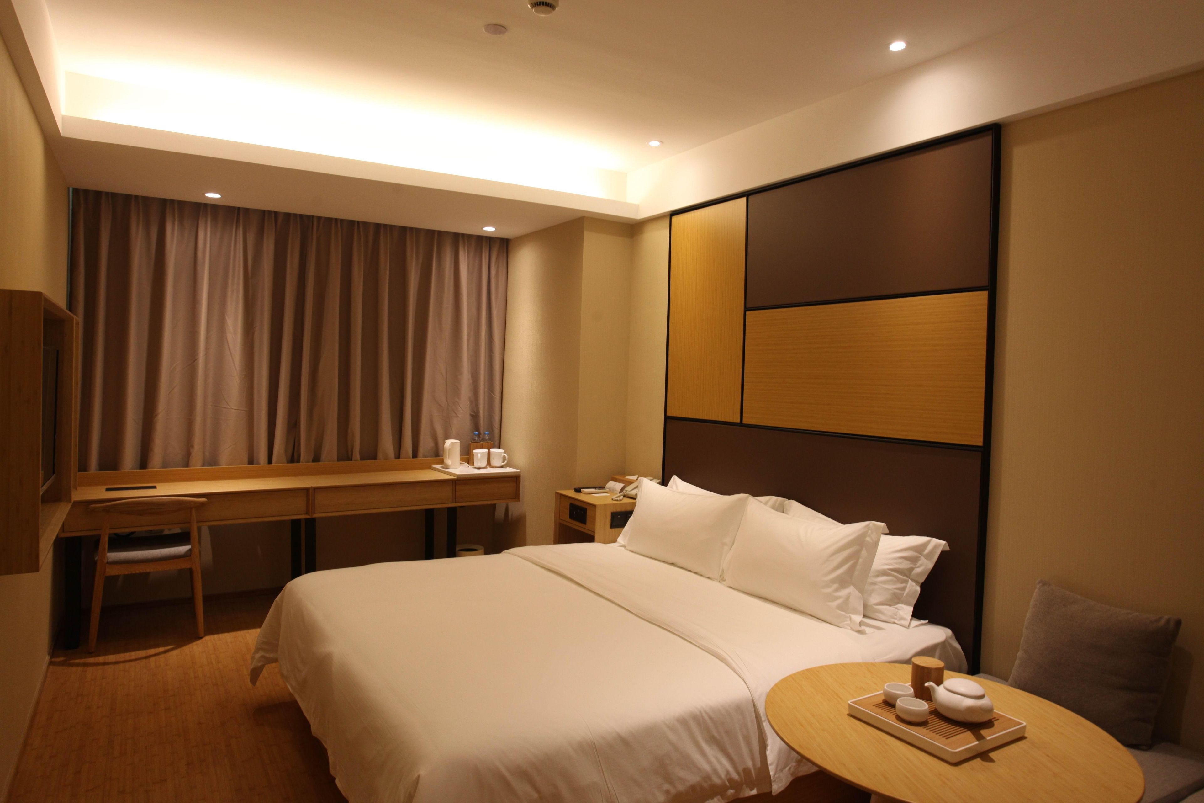 Ein Hotelzimmer mit Bett, Schreibtisch, Stuhl, Nachttisch und einem kleinen runden Tisch mit Tablett.