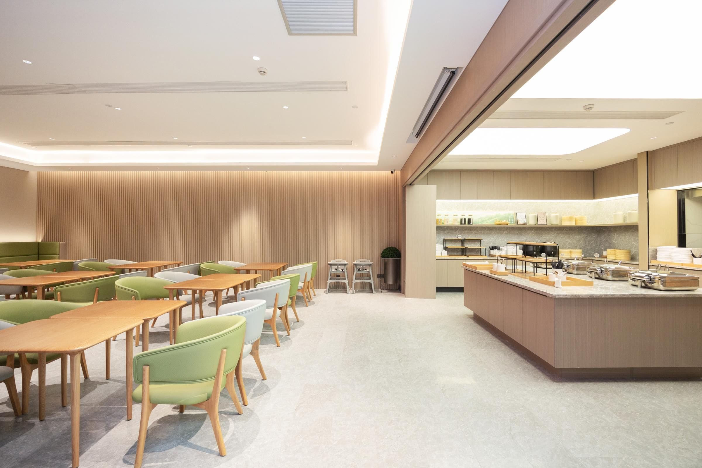 Un espace repas moderne avec des tables et des chaises en bois, un îlot central doté d’appareils de cuisine, et une vue sur la cuisine en arrière-plan.