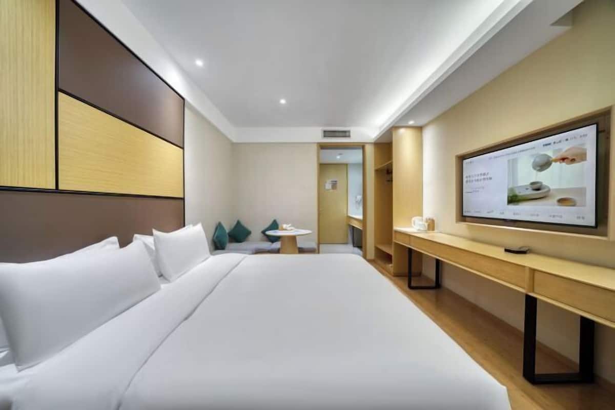 Quarto de hotel com uma cama grande, uma escrivaninha, uma televisão e uma mesa pequena.