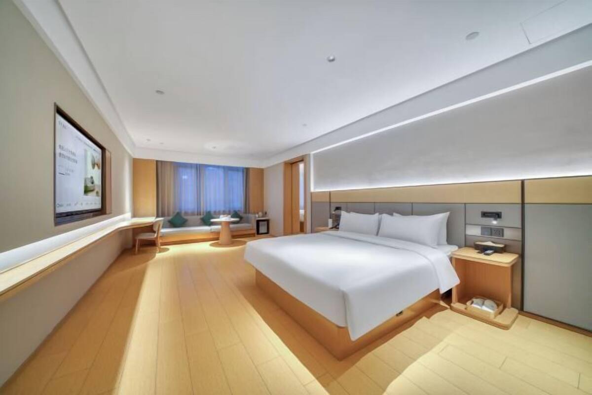 Quarto de hotel moderno com uma cama grande, mesas de cabeceira, uma escrivaninha e um espaço de estar com uma cadeira e uma mesinha.