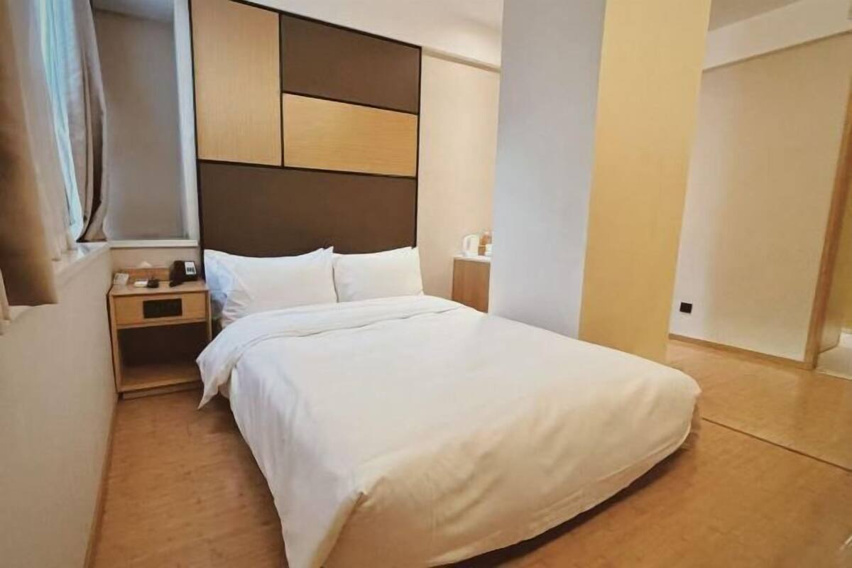 Quarto de hotel com cama, mesa de cabeceira e janela com cortinas.