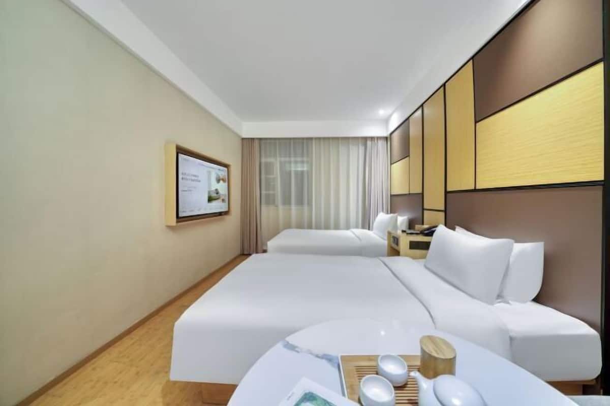 Quarto de hotel com uma cama grande, uma mesa de cabeceira com abajur, uma televisão fixada na parede e um certificado emoldurado.