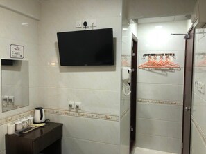 A hotel bathroom with a flat-screen TV mounted above the sink, a towel rack with orange hangers, and a shower area with a glass door. - Wing Lee Guest House (Hong Kong)