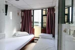 A hotel room with two beds, a window with curtains, a tiled wall, and a view of the outside. - Wing Lee Guest House (Hong Kong)