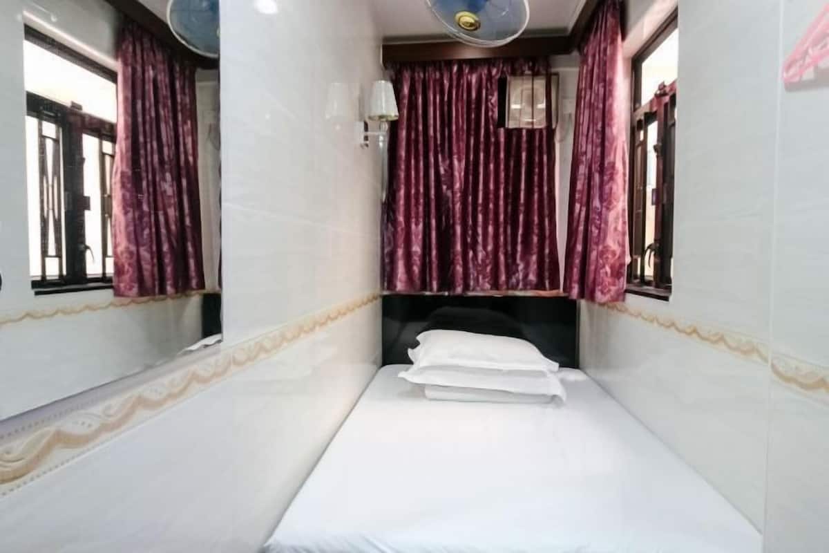A single bed with white bedding, a headboard, and a window with purple curtains.