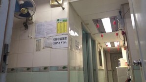 A hallway with a fan, a China Visa sign, and a refrigerator. - Wing Lee Guest House (Hong Kong)