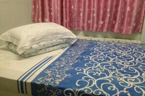 A bed with a patterned bedspread and a pillow, a window with a curtain, and a wall with a light switch. - Wing Lee Guest House (Hong Kong)