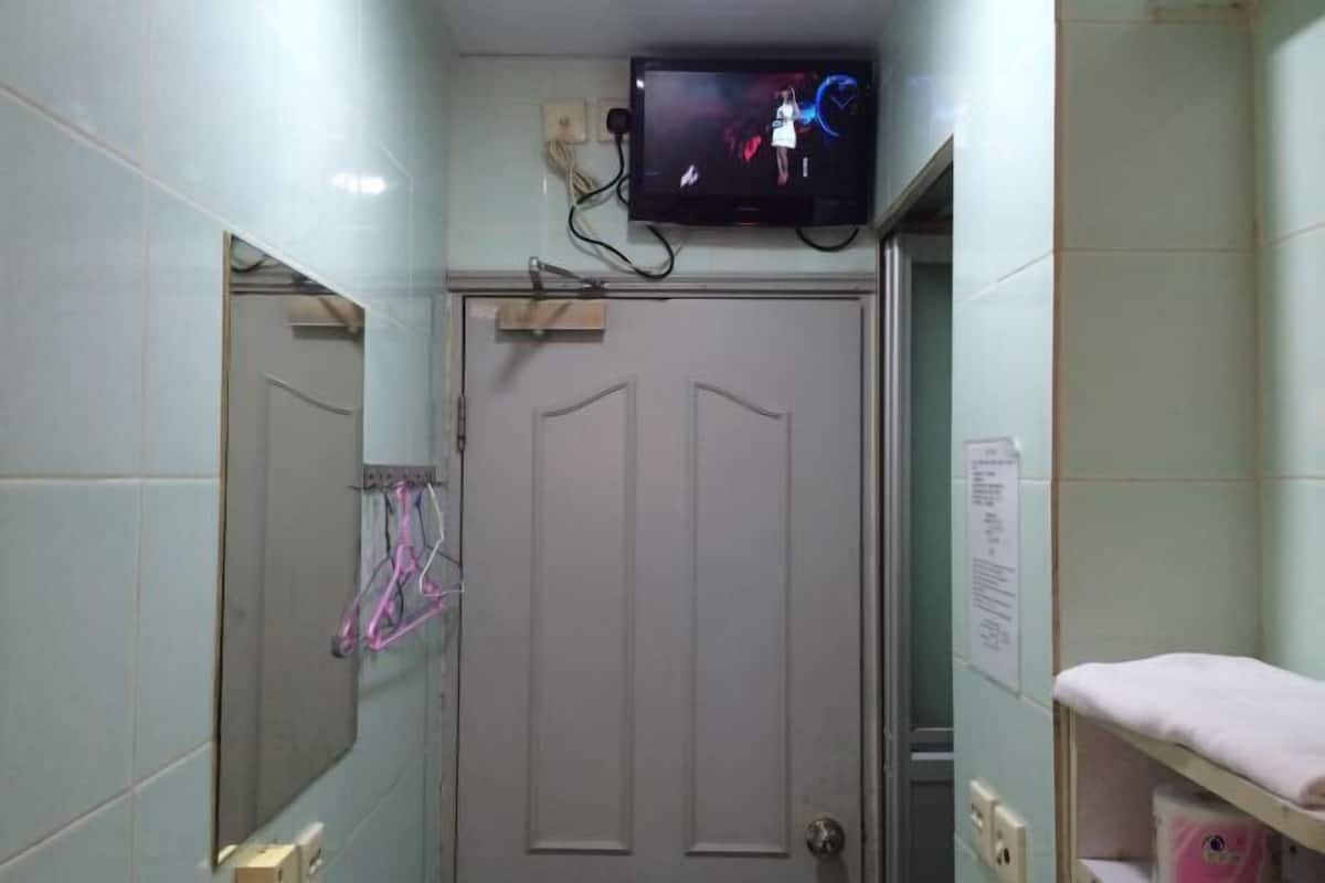 A bathroom with a television mounted above a door, a mirror on the wall, and a shelf with a towel.