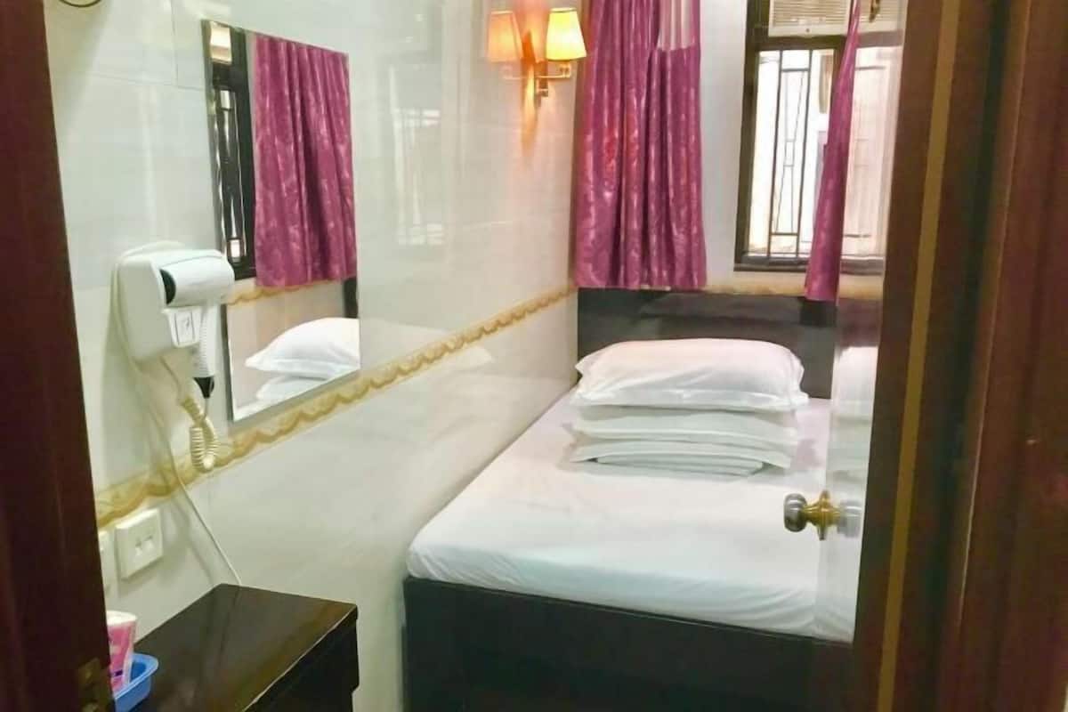A hotel room with a bed, a mirror, a hairdryer, and a window with curtains.