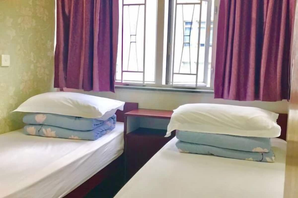 A room with two single beds, a small table, and a window with curtains.