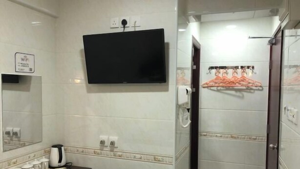 A hotel bathroom with a flat-screen TV, a towel rack, a mirror, and a sink with a dark countertop. - Wing Lee Guest House (Hong Kong)